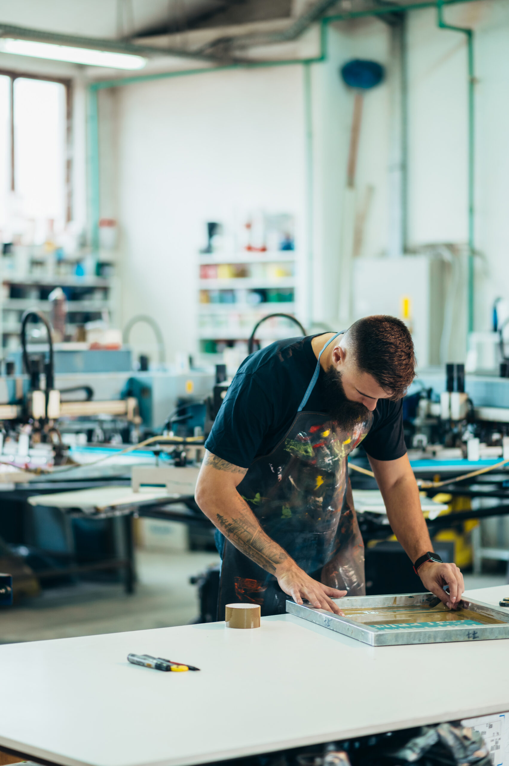 Male worker preparing screen printing film and wearing a dirty apron while working in a workshop