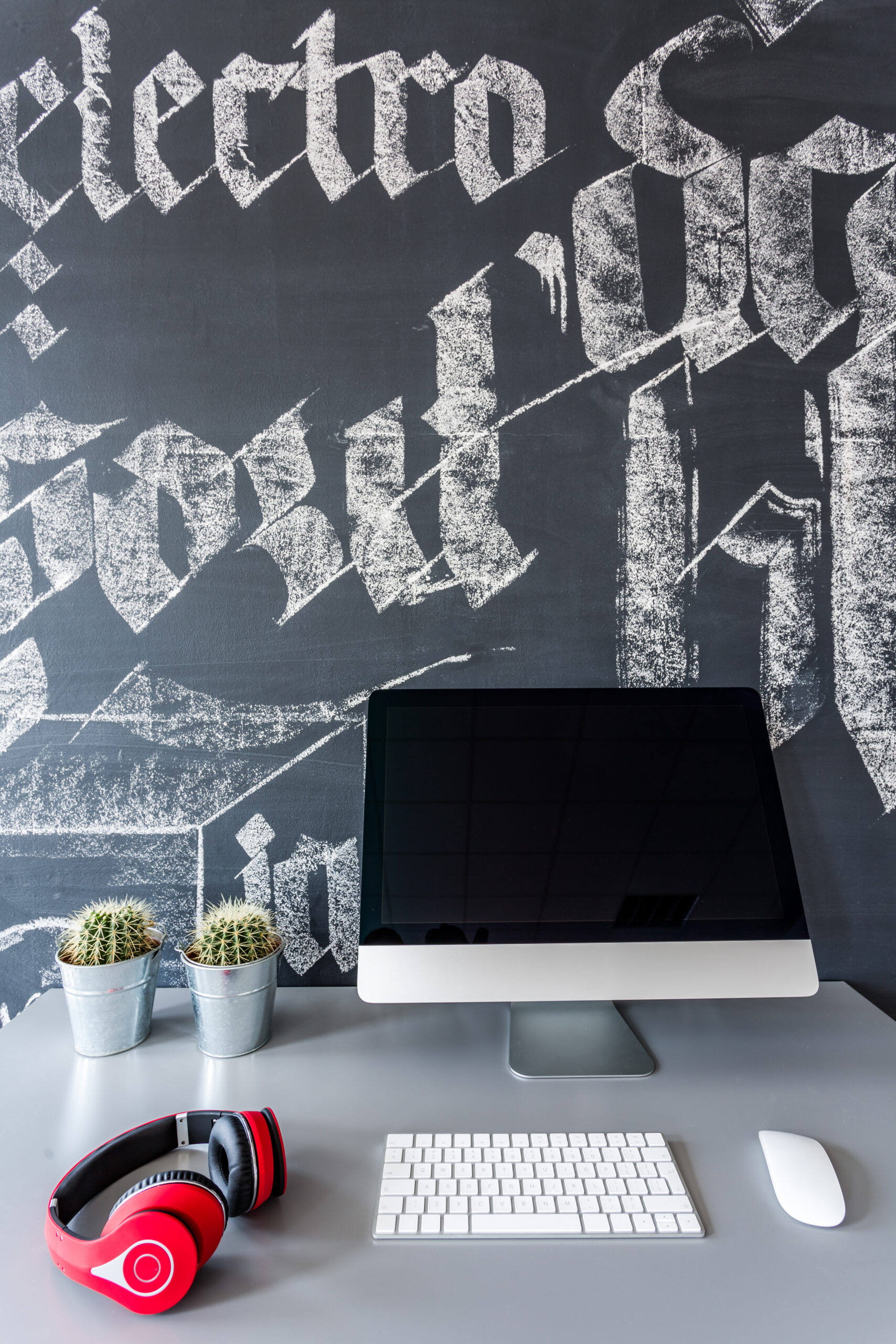 Shot of a desk with a computer and headphones against a chalkboard wall