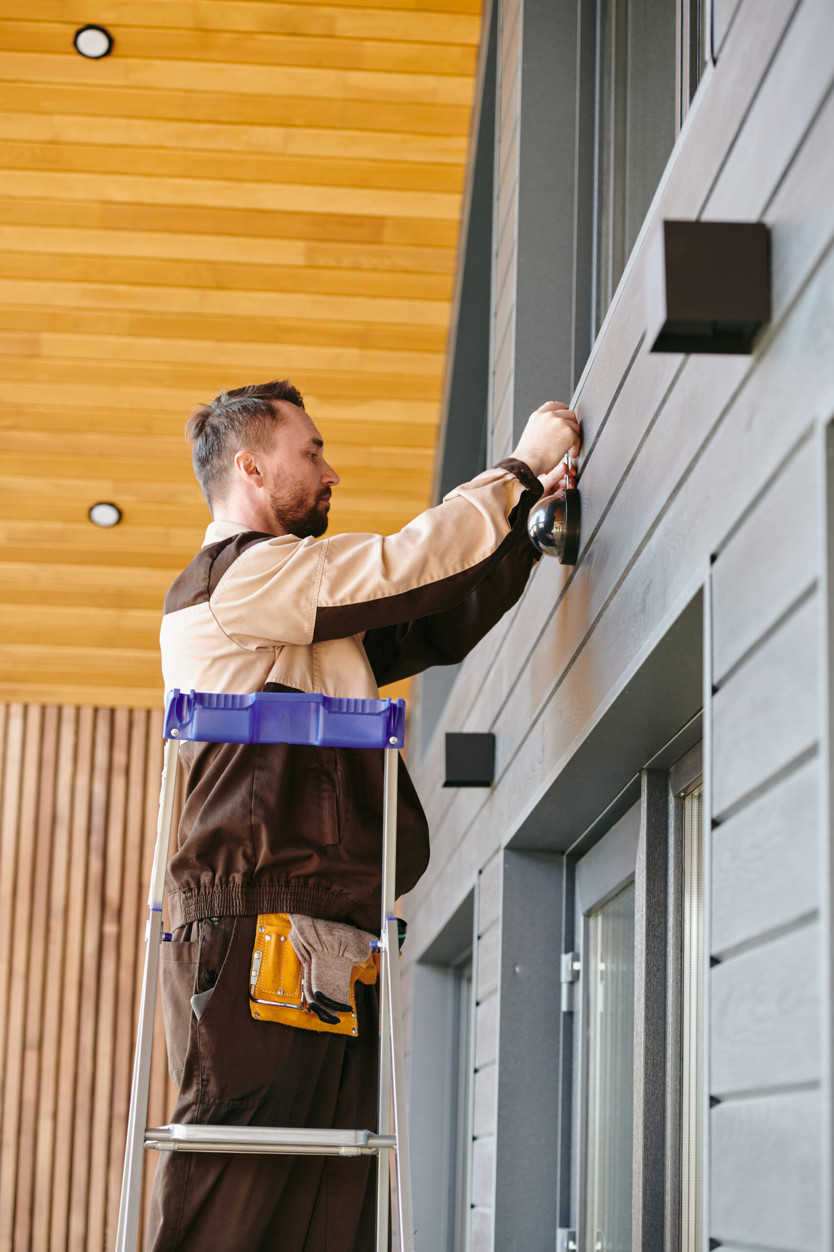 Young man fixing or repairing alarm system while standing on stepladder