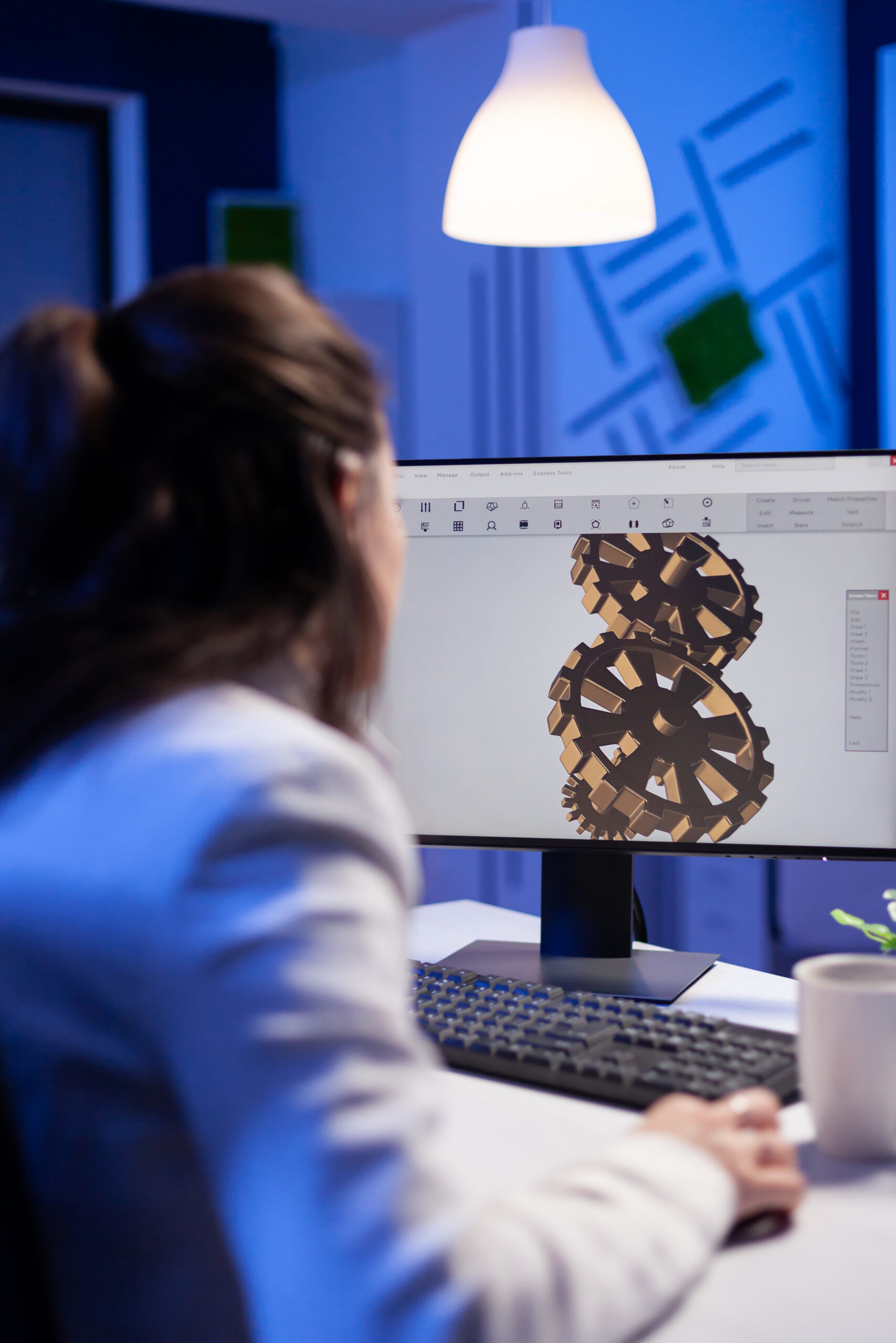 Focused architect working at new project using computer doing gear prototype late at night sitting at desk in start-up office. Industrial woman engineer studying on pc for development cad software